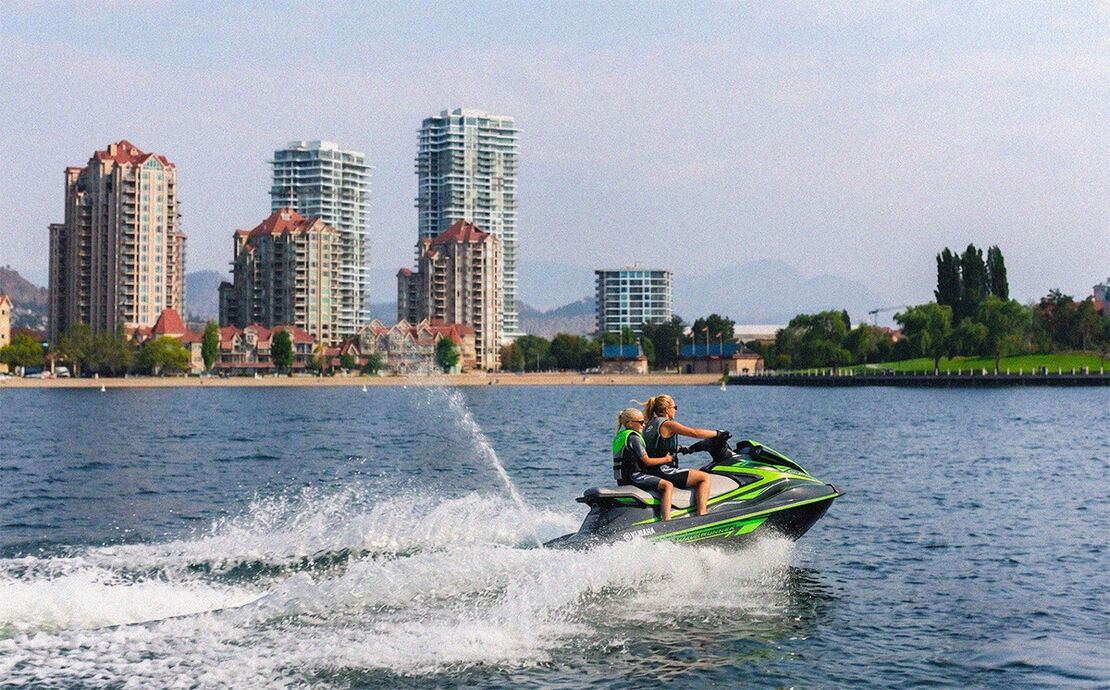 Two up on the Yamaha VX Deluxe Waverunner, Kelowna skyline behind them, Okanagan Lake and adventure ahead.
